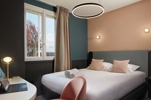 A hotel room with a bed, a desk with a laptop, a chair, and a window with curtains. - Alesia (Beaune)