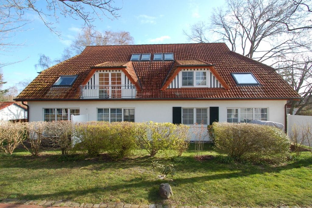 A two-story house with a sloped roof, dormer windows, and a front garden with shrubs.