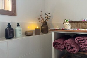 A bathroom with toiletries, a candle, and towels. - Tom's Stuga Holiday Apartment (Schöneiche)