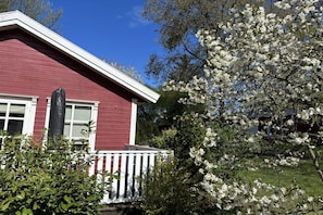A red building with a white porch and a tree with white blossoms in the foreground. - Tom's Stuga Holiday Apartment (Schöneiche)