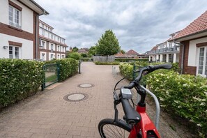 A residential street with a bicycle in the foreground, a gated entrance, and houses with red-tiled roofs. - Friesennest Langeoog (Langeoog)