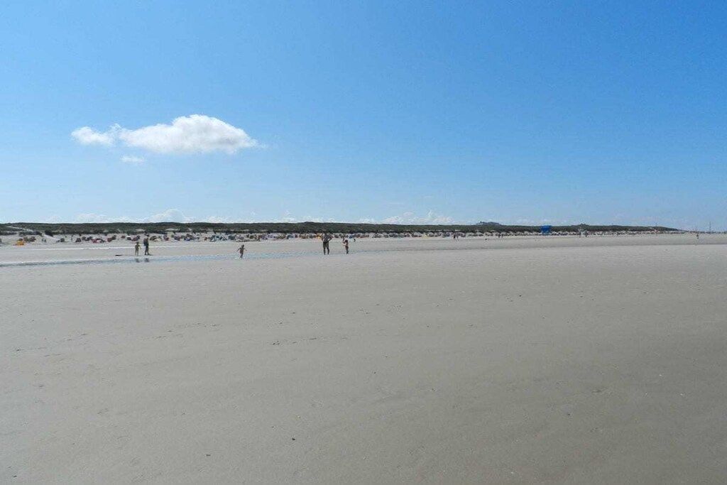 A wide sandy beach with a clear sky and a few people scattered across the sand.