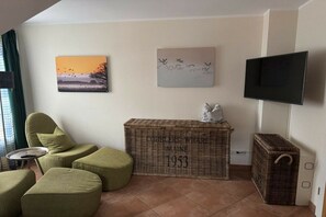 A living room with a sofa, ottoman, a flat-screen TV, and a decorative basket with text. - Holiday home in Zingst with swimming pool (Zingst)