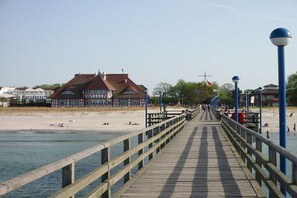 A wooden pier leading to a beach with a building in the background. - Holiday home in Zingst with swimming pool (Zingst)