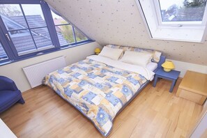 Una camera da letto con soffitto spiovente, un letto con biancheria a motivi, un comodino con una lampada e una finestra vista esterna.
