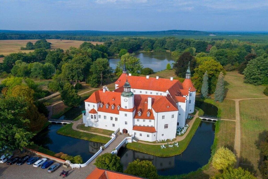 Un grand bâtiment blanc, surmonté d’un toit rouge, entouré d’eau et de verdure.