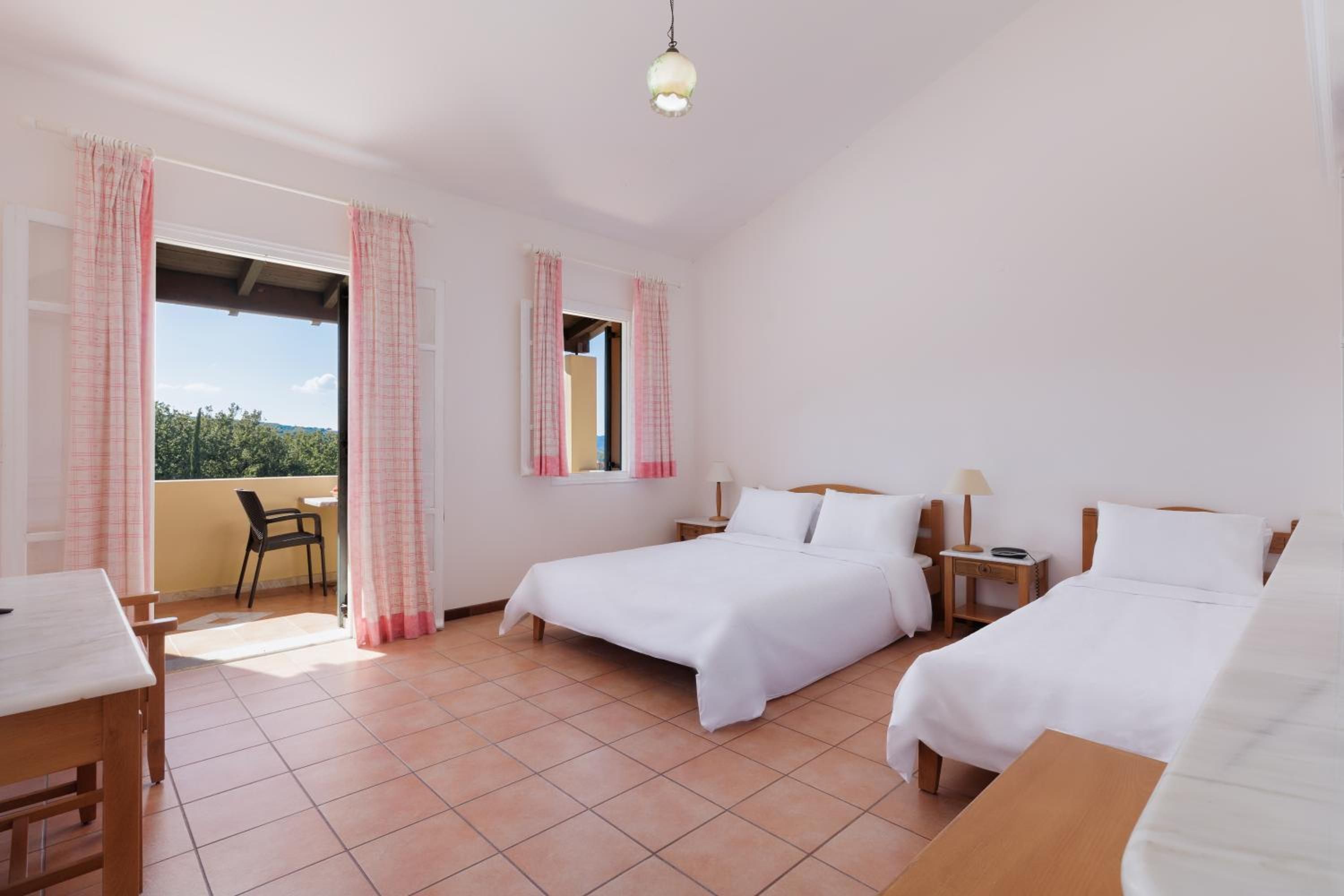 Ein Hotelzimmer mit zwei Betten, einem kleinen Tisch, einem Stuhl, einem Nachttisch und einem Fenster mit Vorhängen.
