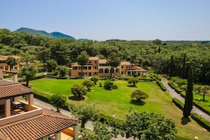 Um edifício grande, com vários andares e um pátio central, rodeado por vegetação exuberante e colinas ao fundo.