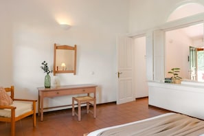 Quarto com uma cama, escrivaninha de madeira, cadeira, espelho e janela com vista.