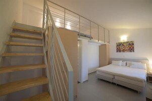 A bedroom with a bed, a staircase, and a wall-mounted artwork.