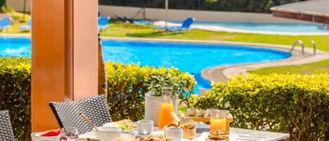 A dining table with breakfast items and a view of a swimming pool.