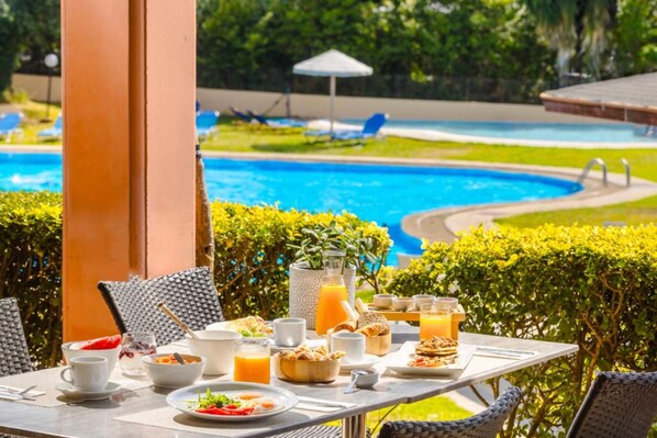 Una mesa de comedor con alimentos para el desayuno y vista a una piscina.