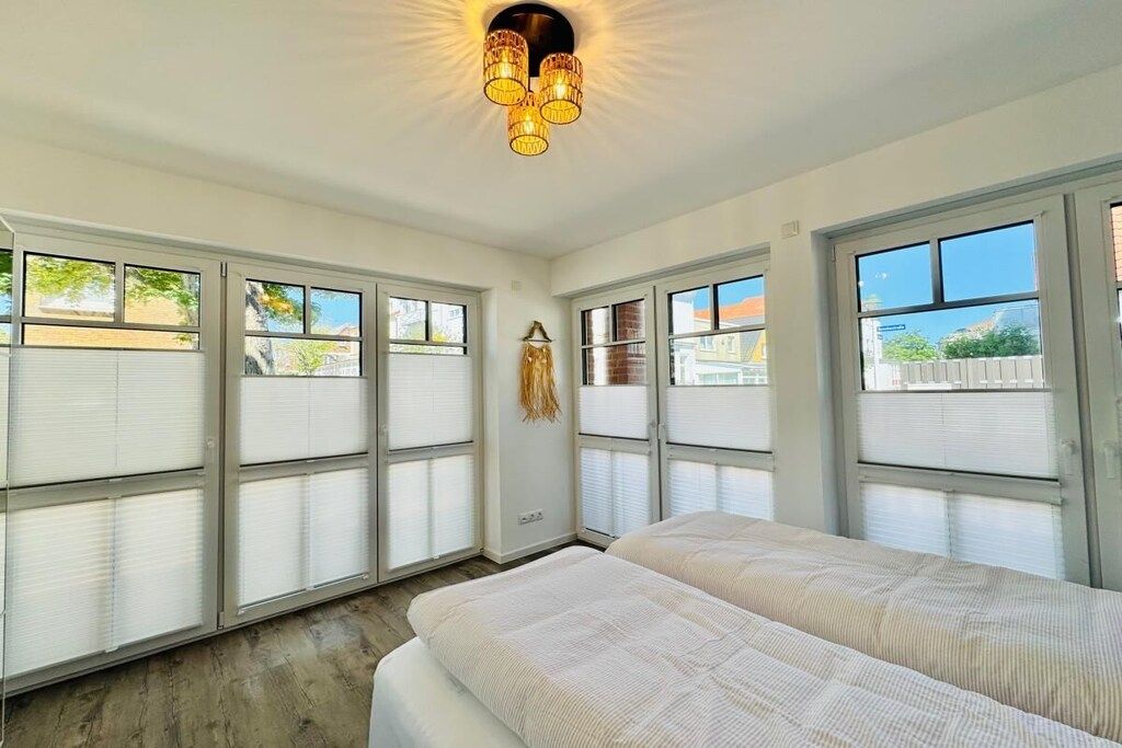 A room with two beds, large windows, and a ceiling light fixture.