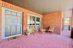 Eine überdachte Terrasse mit Ziegelmauern, einer Schiebetür aus Glas und zwei Holzstühlen.