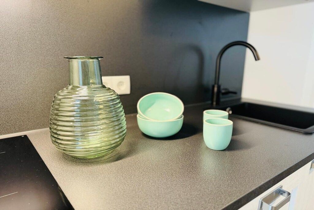 A kitchen counter with a glass vase, two stacked bowls, and two cups.