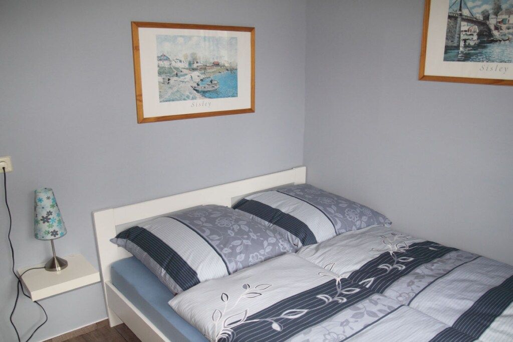 Un dormitorio con cama, mesita de noche, lámpara y dos cuadros en la pared.