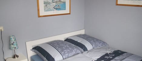A bedroom with a bed, a nightstand, a lamp, and two framed pictures on the wall.