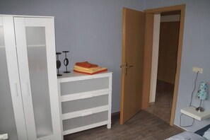 A room with a white wardrobe, a small white table with a lamp, and a wooden door leading to another room. - Holiday apartment in Jabel with swimming pool (Jabel)