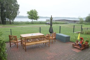 Un patio exterior con mesa y sillas de madera, un banco, una sombrilla y plantas en macetas.