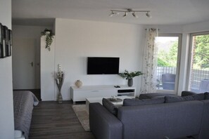 A modern living room with a flat-screen TV mounted on the wall, a grey sofa, a white console table, and a large window with curtains. - Holiday apartment with 2 bedrooms (Stolpe)