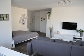 A modern bedroom with a bed, a grey sofa, a TV, and a white console table. - Holiday apartment with 2 bedrooms (Stolpe)