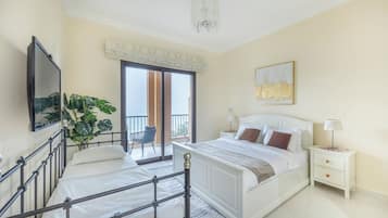 A bedroom with a bed, a nightstand, a chair, a plant, and a view of the outside.