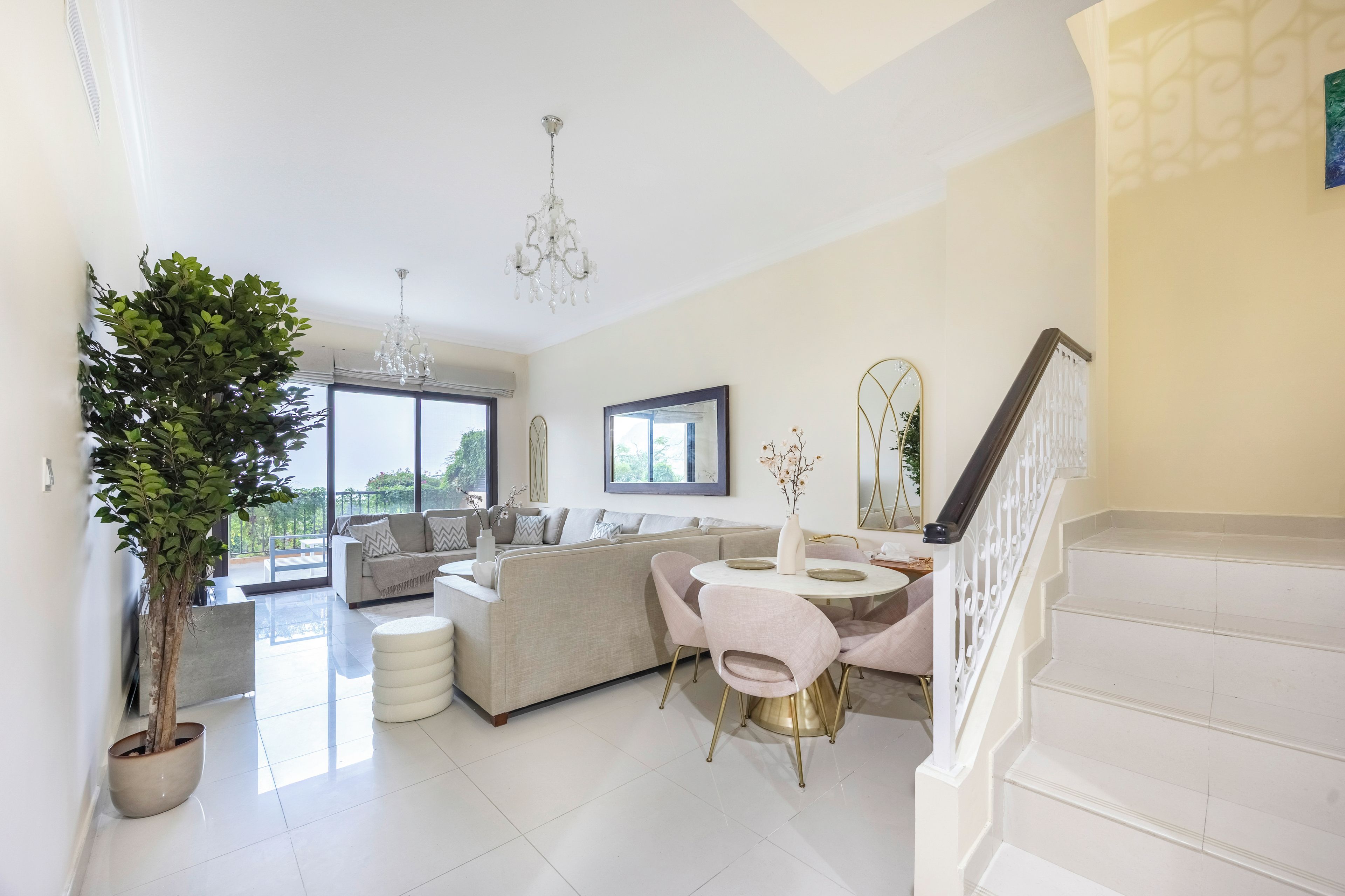 Un vaste espace de vie comprenant un ensemble de canapés, une table à manger avec des chaises, un escalier et une grande fenêtre donnant sur un paysage verdoyant.