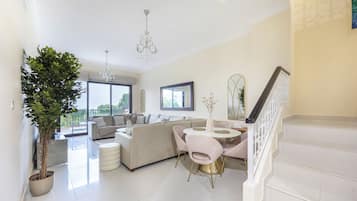 Un vaste espace de vie comprenant un ensemble de canapés, une table à manger avec des chaises, un escalier et une grande fenêtre donnant sur un paysage verdoyant.