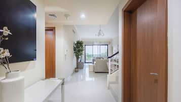 A modern interior with a white tiled floor, a wooden door, a white console table, and a potted plant.
