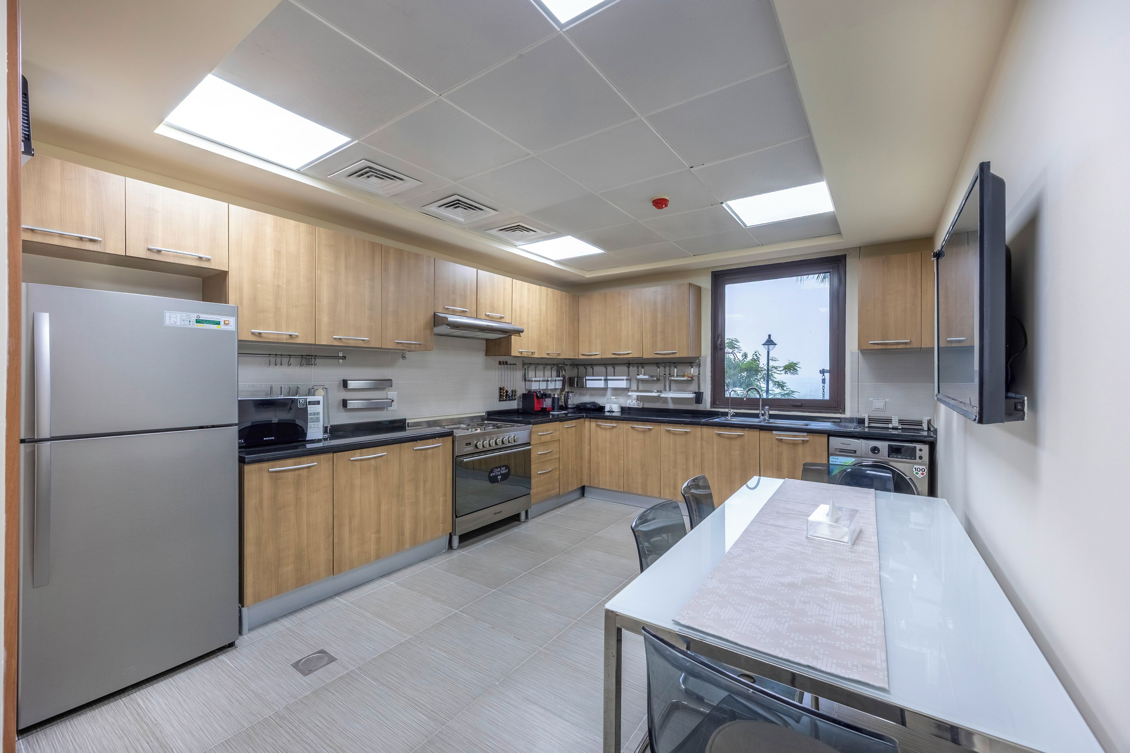 A modern kitchen with stainless steel appliances, wooden cabinets, and a large window.