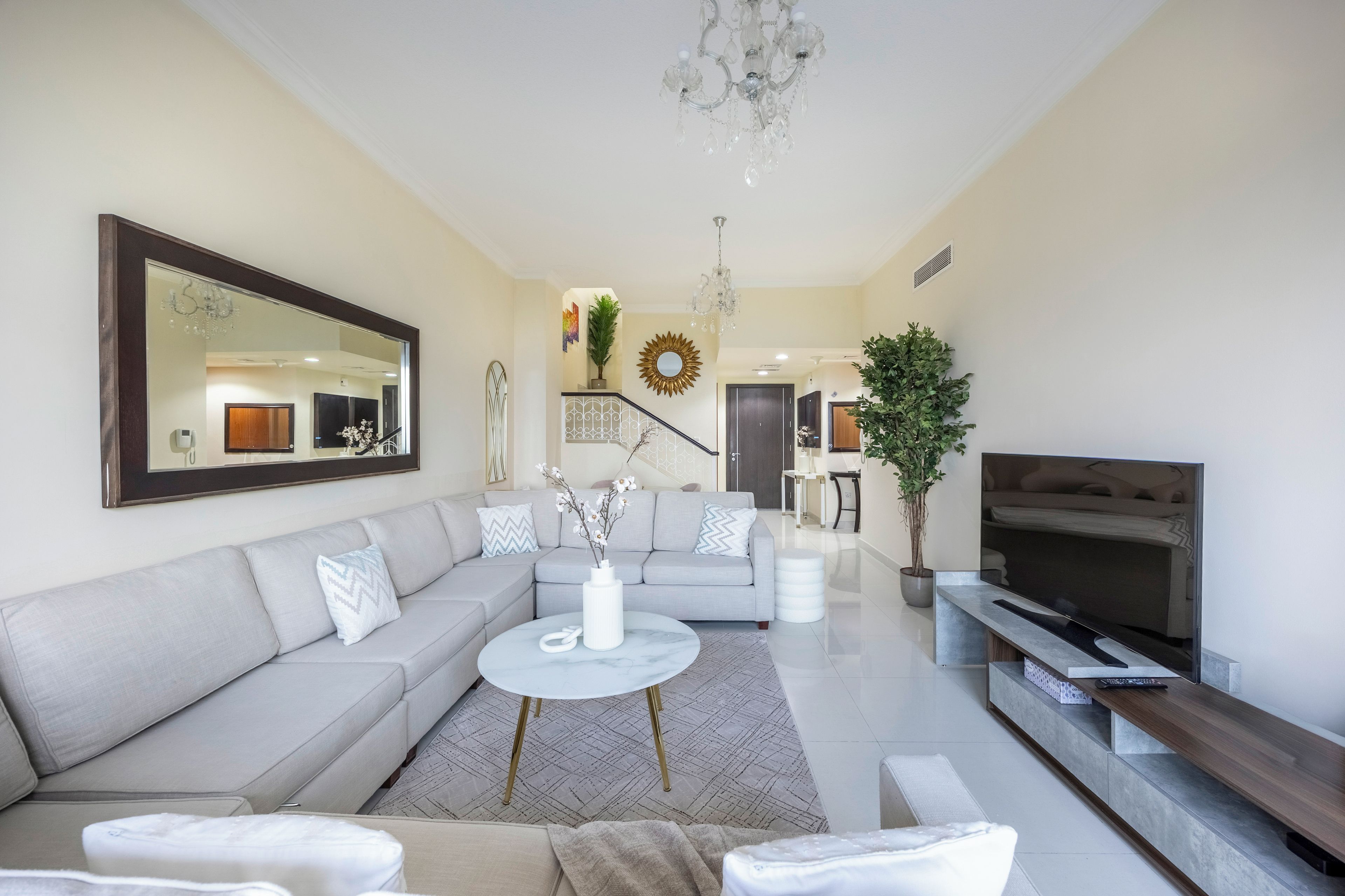 A modern living room with a grey sofa, a coffee table, a TV, and a chandelier.