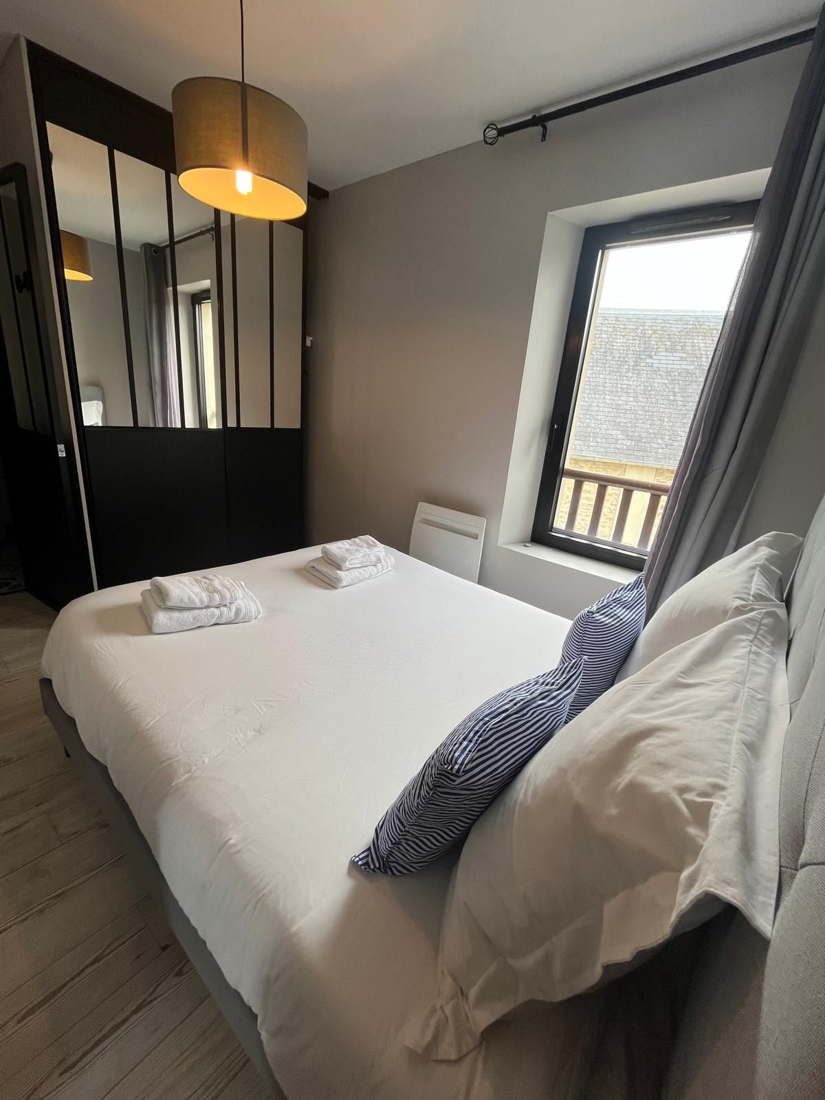 Habitación de hotel con una cama grande, ventana con vistas, lámpara colgante y un espejo.