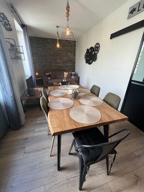 A dining area with a wooden table, black chairs, and woven placemats. - Harbor Master's Office—stunning harbor view—downtown (Port-en-Bessin-Huppain)