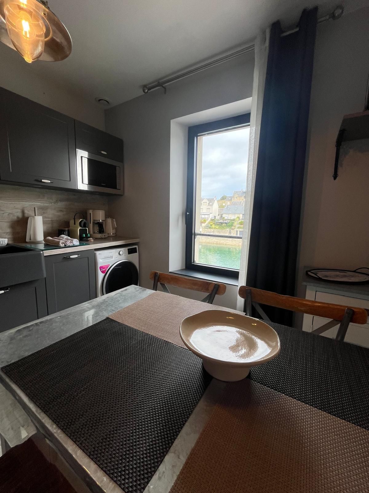 Una cocina compacta con electrodomésticos modernos, un comedor con mesa y sillas, y un ventanal con vistas al exterior.