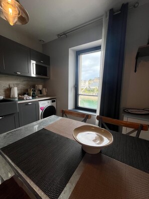 A compact kitchen with modern appliances, a dining area with a table and chairs, and a window with a view of the outside. - Harbor Master's Office—stunning harbor view—downtown (Port-en-Bessin-Huppain)