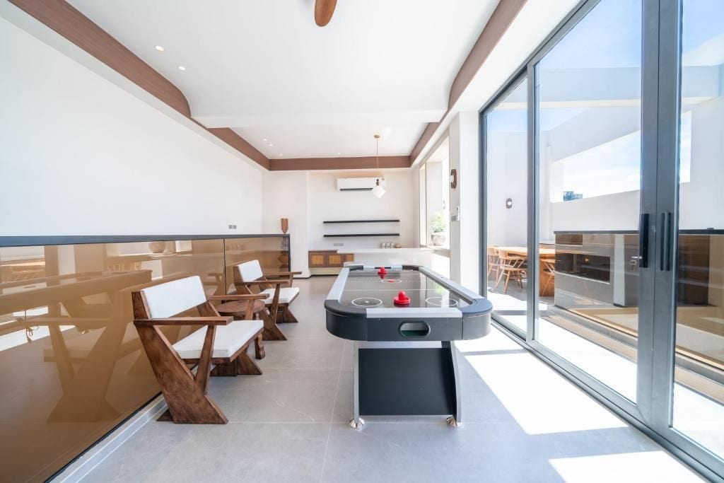 A modern indoor space with a foosball table, seating area, and large windows.