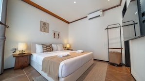 Habitación de hotel con cama, mesitas de noche, aire acondicionado de pared, perchero para toallas y un pequeño adorno en la pared.