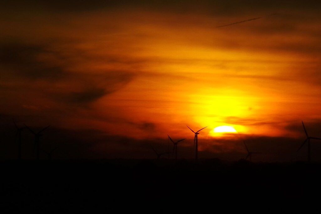 Een zonsondergang met een silhouet van windturbines tegen een donkere lucht.
