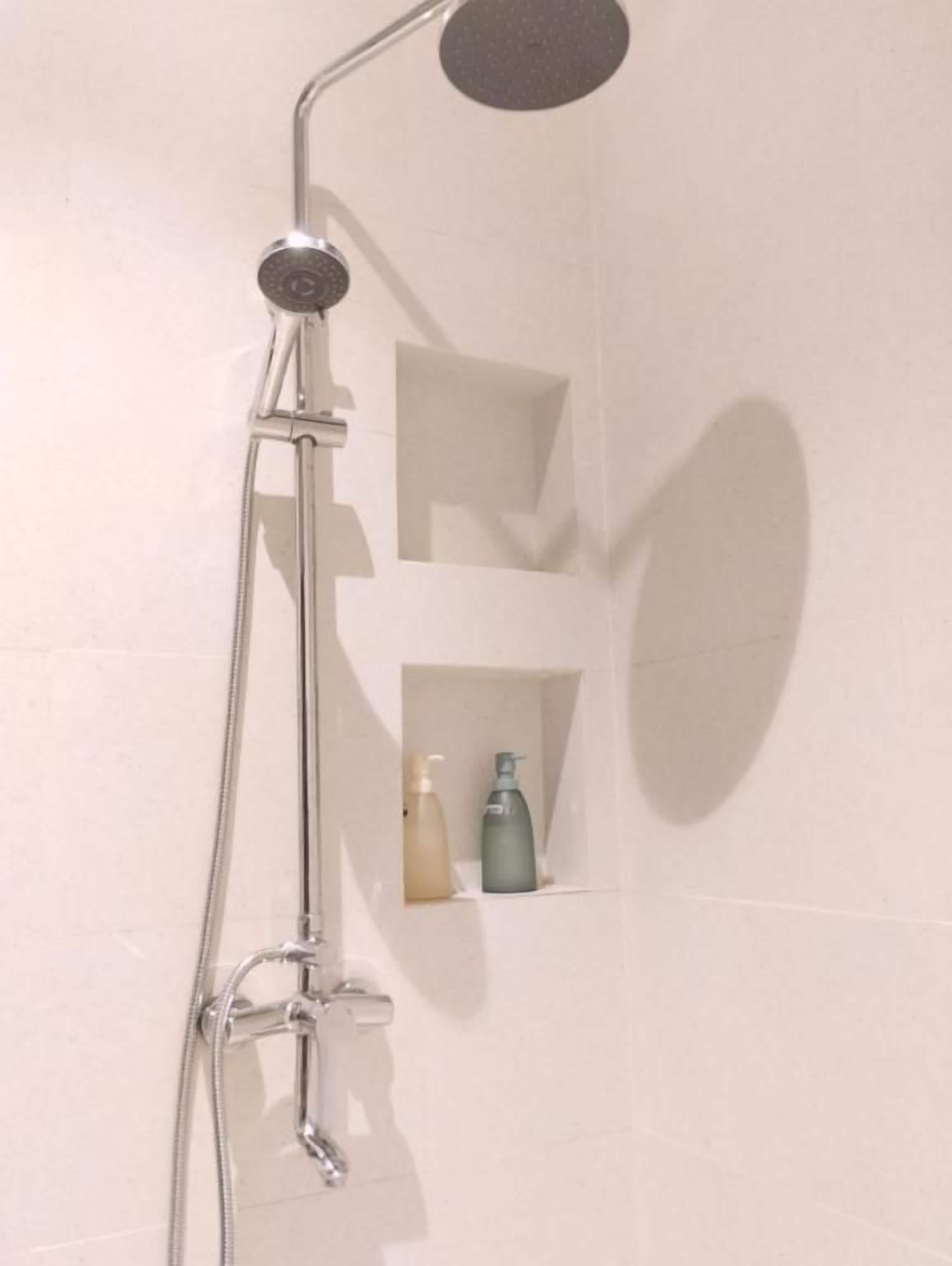 Une douche équipée d’un pommeau de douche à main et d’un robinet mural.