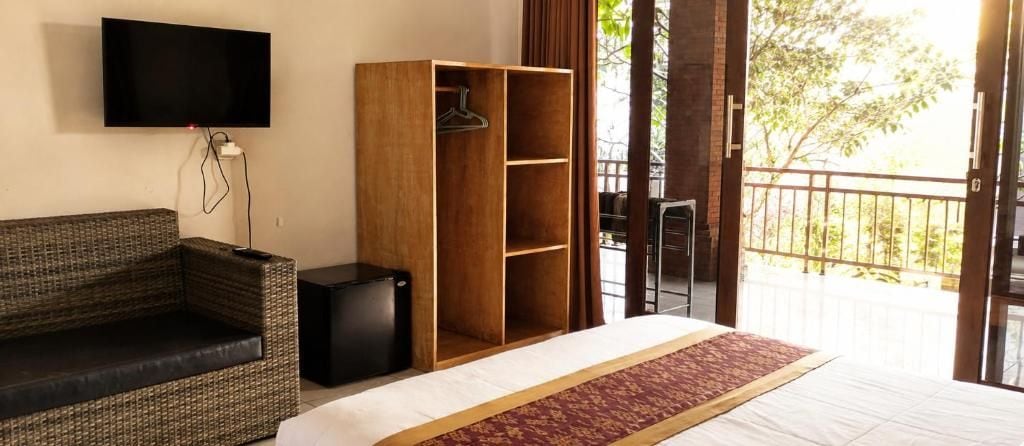 A room with a bed, a television mounted on the wall, a wardrobe, and a balcony with a view of trees.