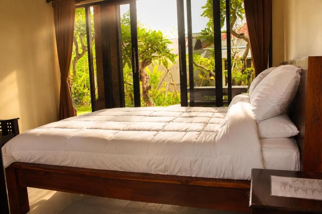 A bed with a white duvet and pillows, a wooden headboard, and a window with curtains.