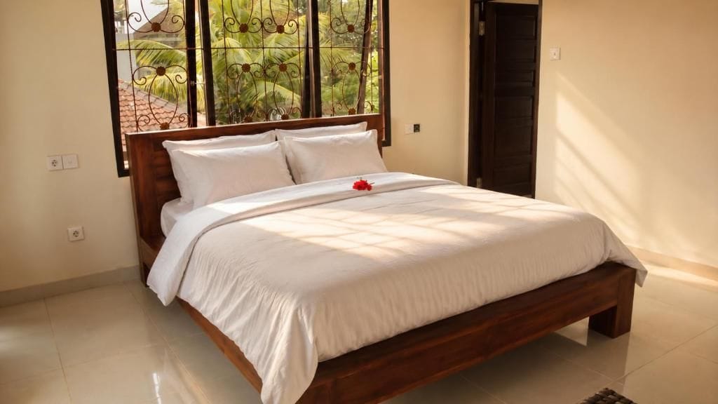 A neatly made bed with a white duvet and pillows, a wooden headboard, and a window with a view of greenery.