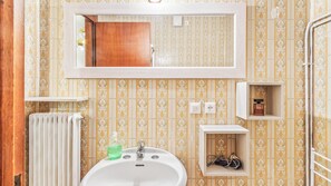 Ein Badezimmer mit Waschbecken, Spiegel, Handtuchhalter und Duschbereich.