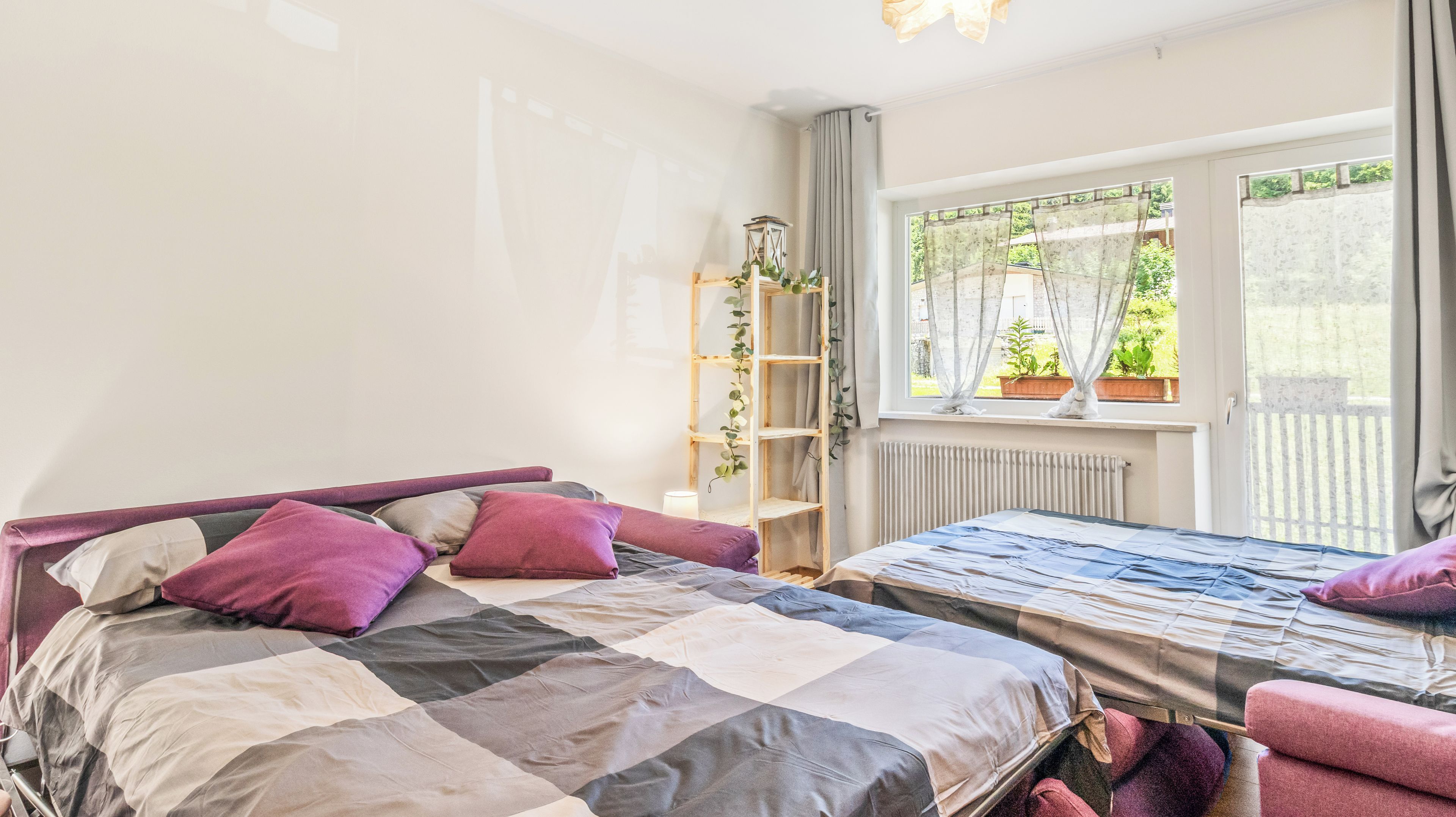 Una camera da letto con un letto, un comodino, una sedia, una finestra con tende e un termosifone.