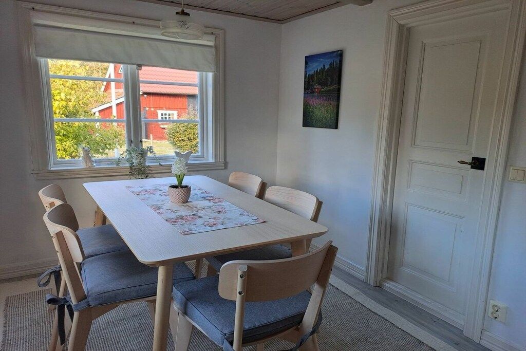 A dining area with a table and chairs, a window with a view of a red building, and a door with a painting above it.