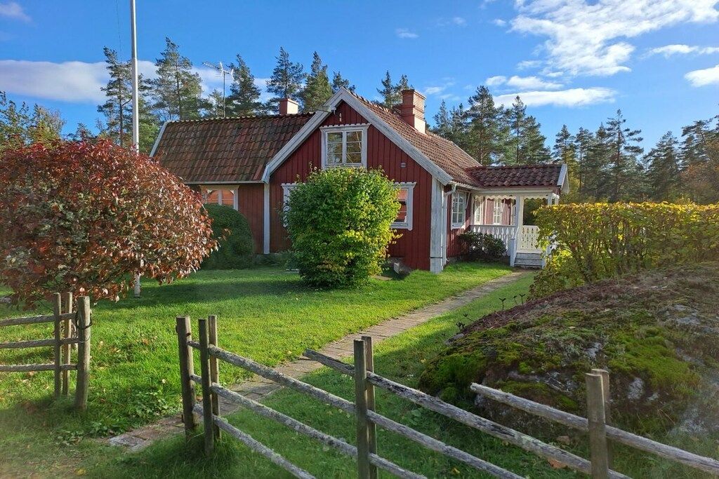 Een rode houten woning met een witte veranda, omringd door een houten hek en begroeiing.