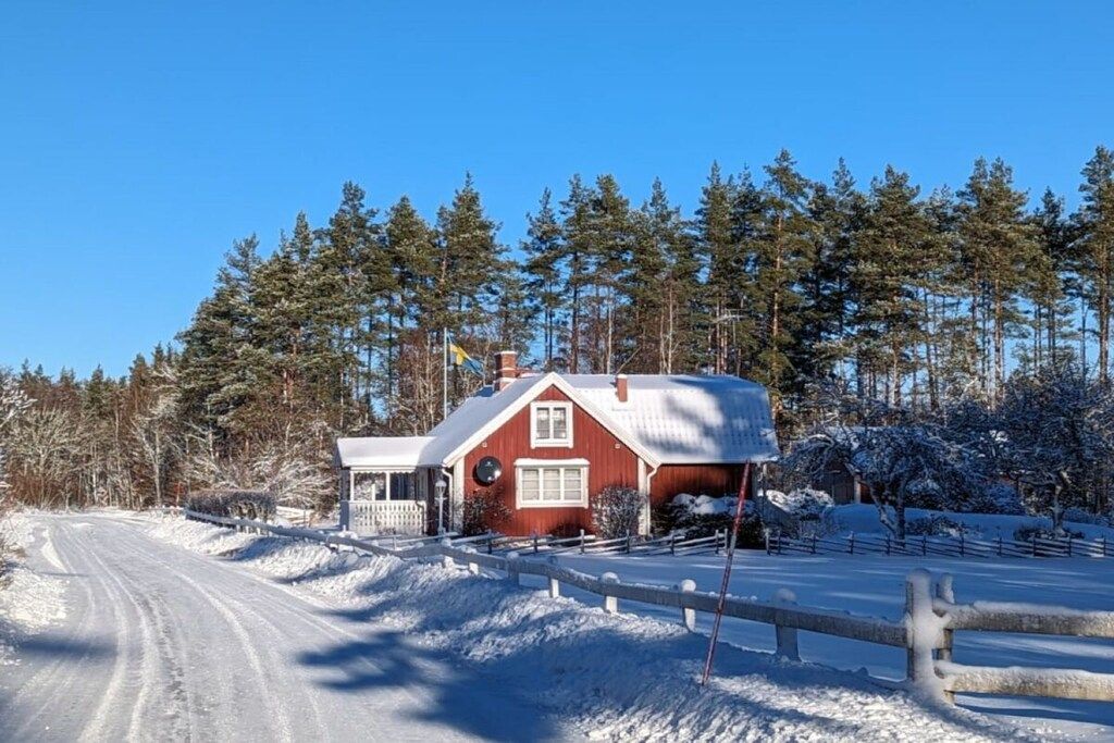 A red house with a snow-covered driveway and a wooden fence.