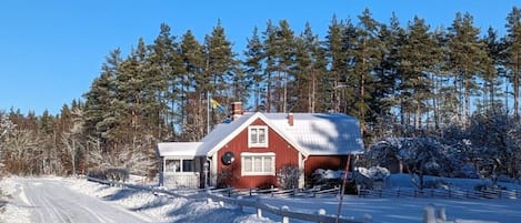 A red house with a snow-covered driveway and a wooden fence.