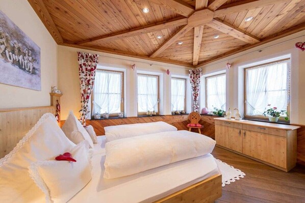 A bedroom with a wooden ceiling, a bed with white bedding, a wooden cabinet, and a window with floral curtains. - Holiday apartment in Schönwald with barbecue (Schönwald)