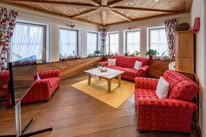 A room with a wooden ceiling, a red patterned sofa set, a wooden coffee table, and a television on a stand. - Holiday apartment in Schönwald with barbecue (Schönwald)